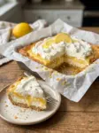 Lemon cream cheese dump cake cut into squares with a creamy lemon layer and whipped cream topping, with a lemon slice on top