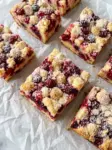 Squares of cranberry Christmas cake with whole cranberries and golden streusel topping dusted with powdered sugar on parchment paper