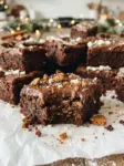 Fudgy holiday gingerbread brownies topped with chocolate frosting and crushed gingerbread cookie crumbs on parchment paper
