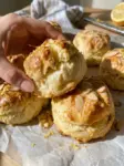 Golden lemon almond cream scones topped with sliced almonds and lemon zest, one held in a hand