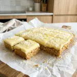 Lemon weet-bix slice cut into squares with lemon icing and coconut on baking paper