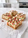 No bake sugar cookie bars with a crumb crust, creamy sprinkle filling, and marshmallow, pecan, and sprinkle topping on parchment