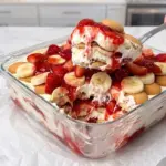 Spoonful of strawberry banana pudding layered with vanilla wafers, bananas and strawberries in a glass dish